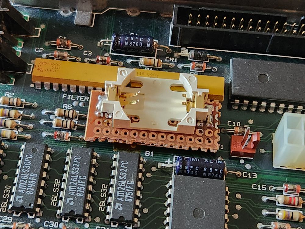 A CR2032 battery holder soldered to a piece of perf board sitting on top of the motherboard.