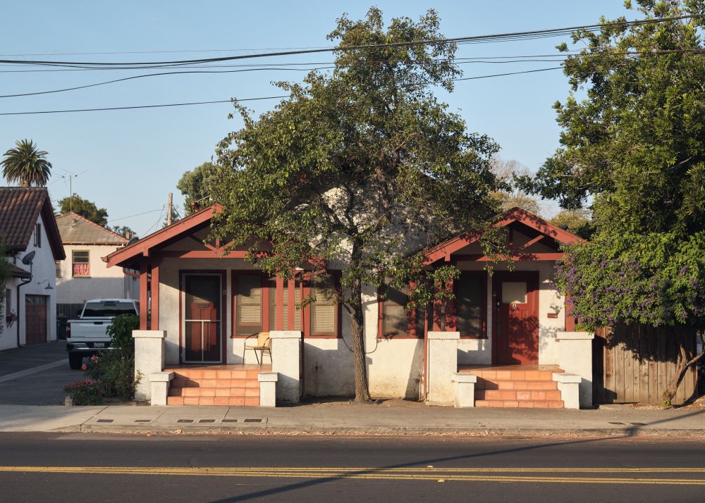 Photo of duplex house in golden light with a tree between the two units doors.