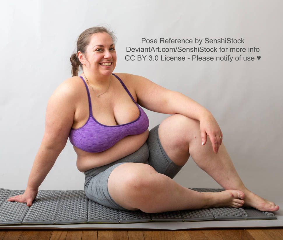 A fat white woman sitting on the floor and smiling, one arm up on her bent knee, the other propping her up.