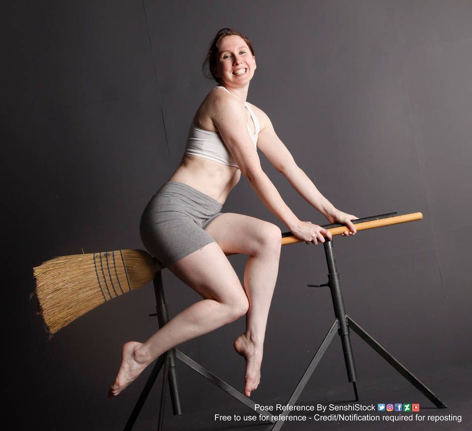A white woman sitting side-saddle on an old wicker style broom. She is holding on to the broom with both hands and smiling at the camera.