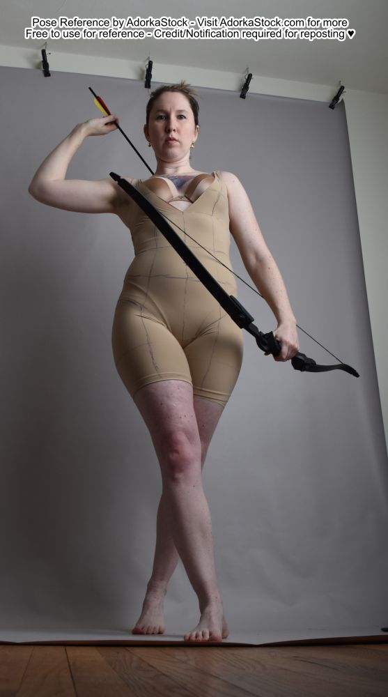 Low angle photo of a thin, white, female model holding a bow and taking a step towards the camera while drawing an arrow from her back 