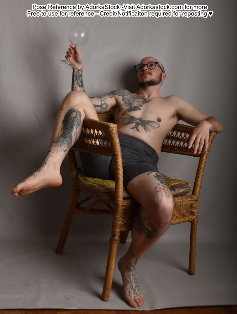 thin male model draped on a chair with one leg up, holding an empty wine glass 