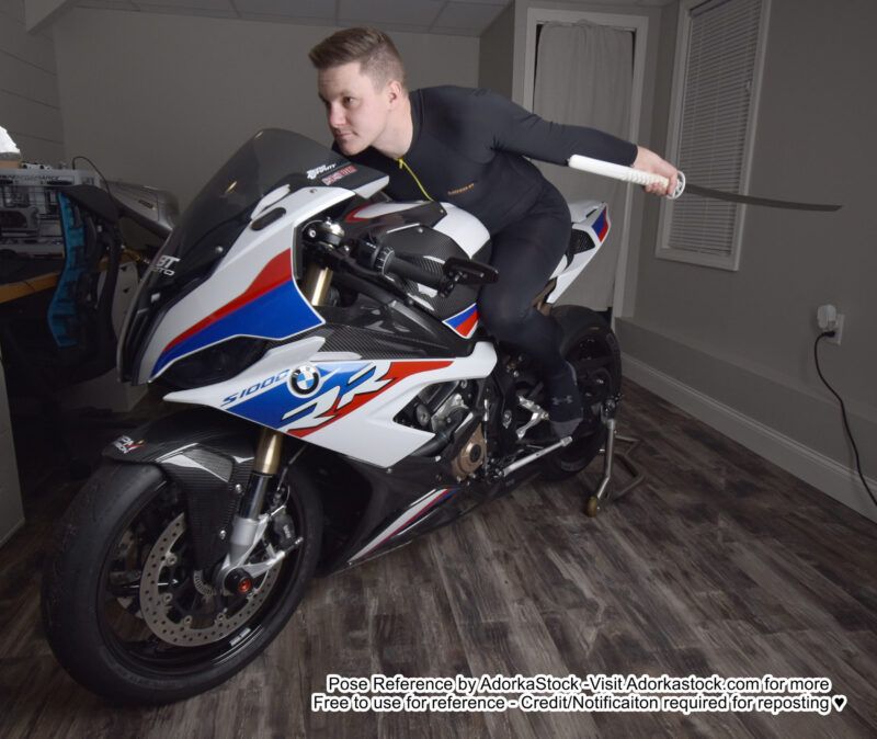 A white man on a motorcycle, holding out a katana as if driving and getting ready to slice.