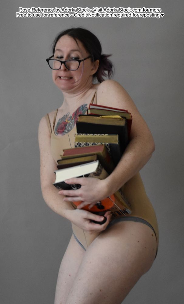 thin white bespectacled female model holding many books that seem like maybe too many, its a struggle 