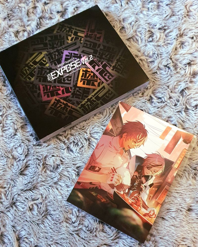 Cd-levy ja kuvakortti jossa kaksi hahmoa syömässä, toisella valtava kulho riisiä ja edessä padassa jotain liskonjalkoja, toisella puikoissa pieni liskonjalka ja ilme hämmentynyt