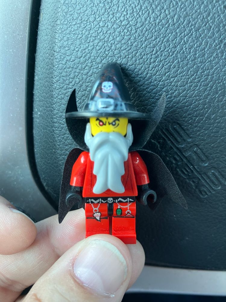 LEGO minifig of a red clothes, black cape wizard with a gray beard and a black hat with a skull on it