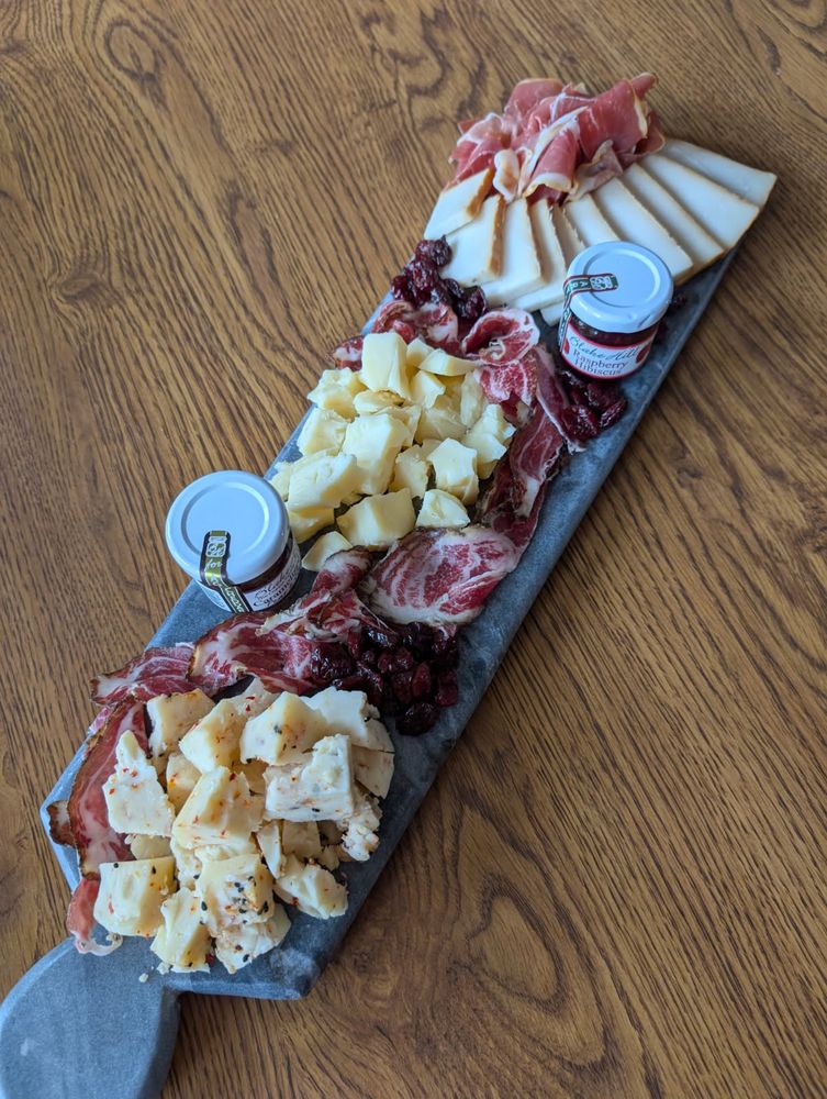A long, narrow stone slab serving board, filled to the brim with a crumbled togarashi cheese, crumbled aged Gouda, a sliced smoked goat cheese, a pile of prosciutto, a river of coppa, dried cherries, and two mini jams (one caramelized pear and honey, the other raspberry hibiscus). 