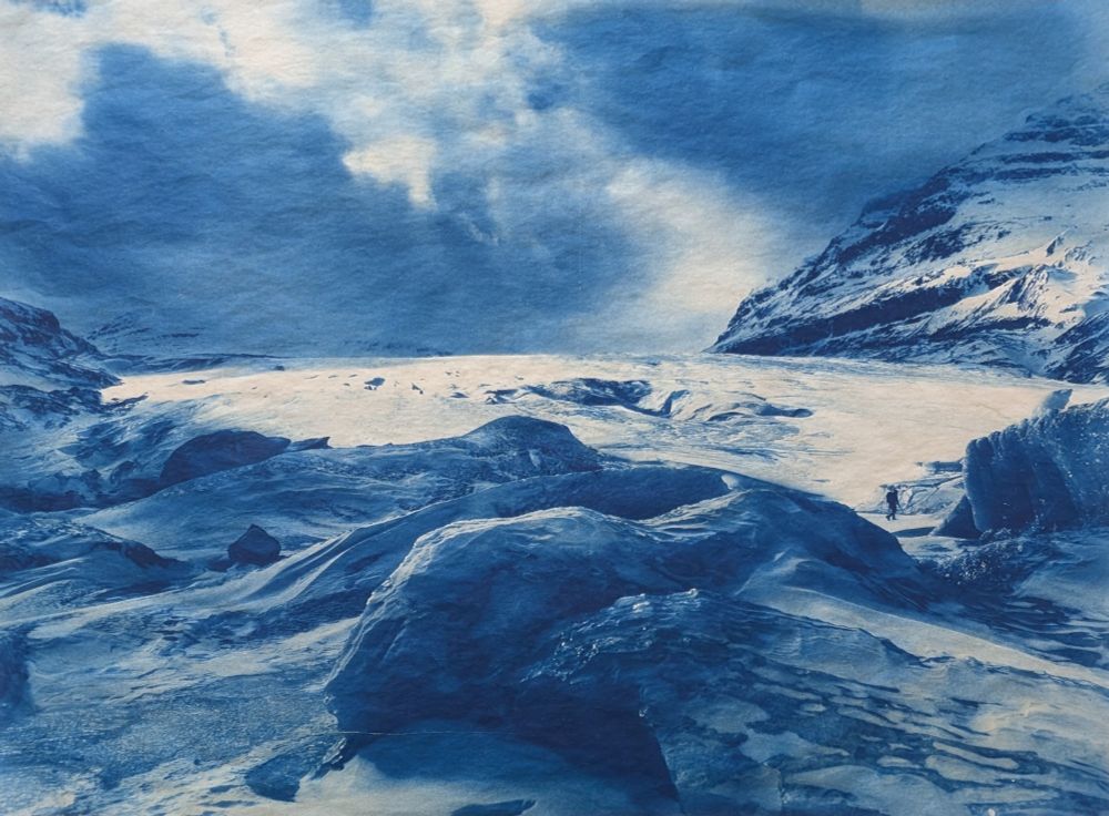 20x26 inch large format cyanotype, printed on mitsumata washi and mounted with chincolle techniques. 

The deep Prussian blue matches with the subject matter of the photo. A large brightly lit glacier with just a hint of sun on it (Saskatchewan glacier, Alberta Canada) sits in the background, with stormy clouds. In the foreground large sheets of ice buckle up (a frozen lake). A very small mountaineer with ice ax is just visible walking between two larger frozen icebergs calved the summer before. Perfect timing for both sun and figure. 