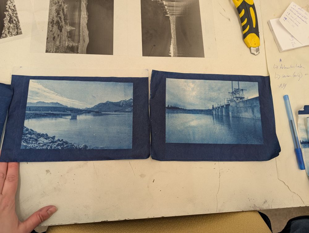 A hand and pen sit by the blue cyanorypes for scale, small versions of the final prints. The lake side of bighorn Dam is shown on the left and the lake side spillway on the right. The water level is at least 25 ft higher than the last time I was there. Photos taken Oct 2024