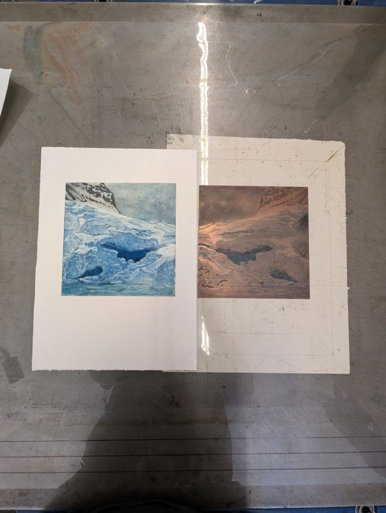 The print and plate are sitting together, a mirrored image of copper on the right and the print on the left. The image shows a black mountain in the distance, and an ice cave with large chunks of ice and glacial debris fallen in front of the wall of ice.