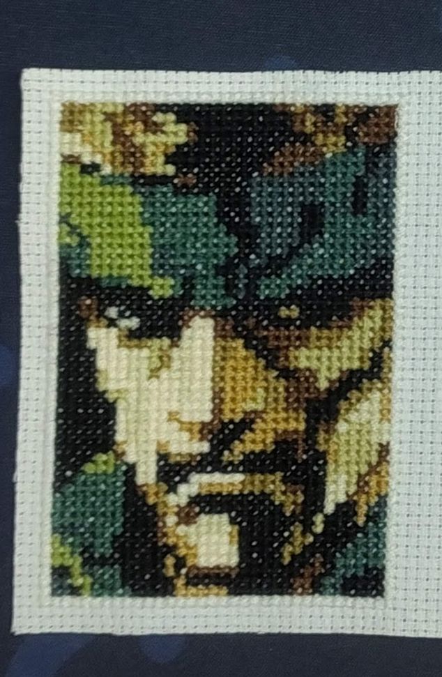 the same MG2 Snake portrait, now in cross-stitch form