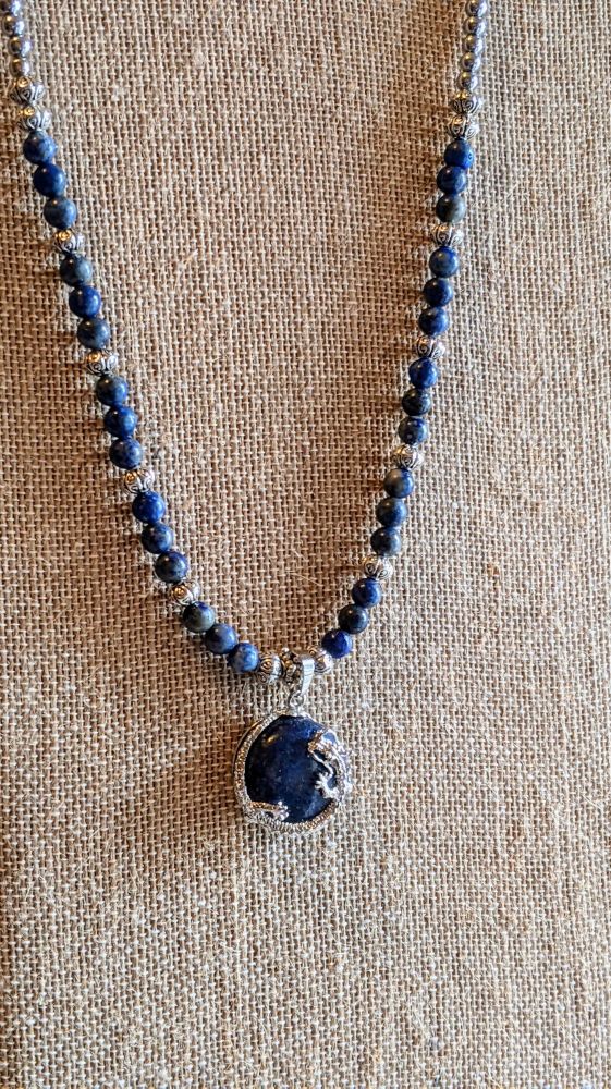 Beaded necklace with lapis lazuli beads with silver accents and a pendant which is a silver dragon wrapped around a lapis marble. 
