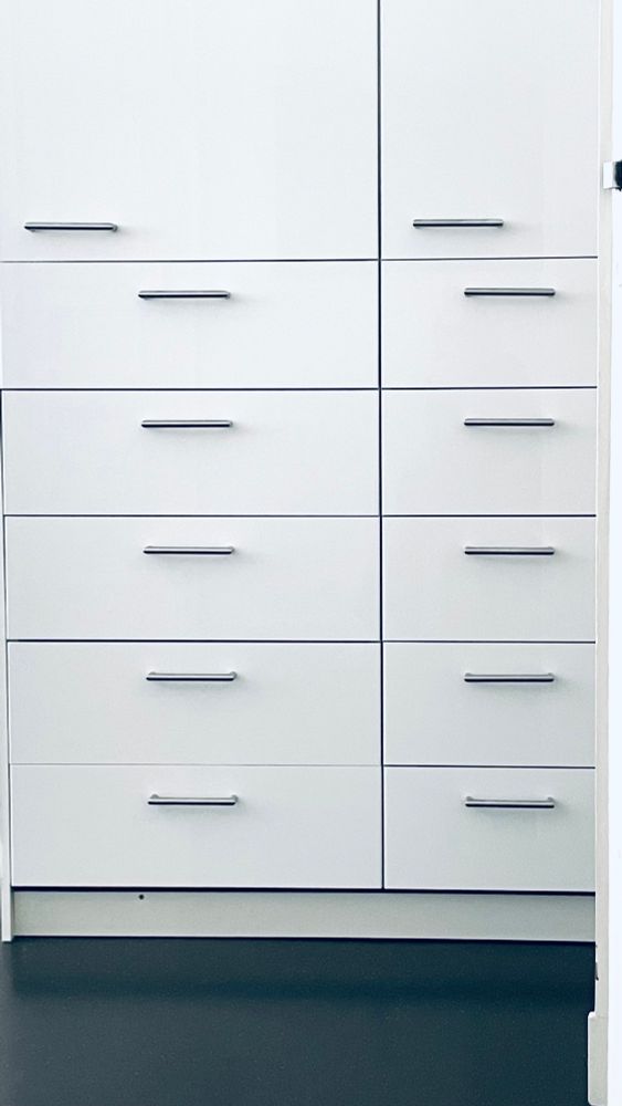Ein Schrank, weiße Türen, viele Griffe. Unten insgesamt 10 Griffe für 10 Schubladen ordentlich in zwei Reihen von fünf neben- und übereinander. Darüber zwei letzte Griffe für Schranktüren. Beide sind jeweils ein Stück nach links versetzt zu den anderen Griffen und dann noch untereinander in unterschiedlich viel, wenn ihr versteht was ich meine. 