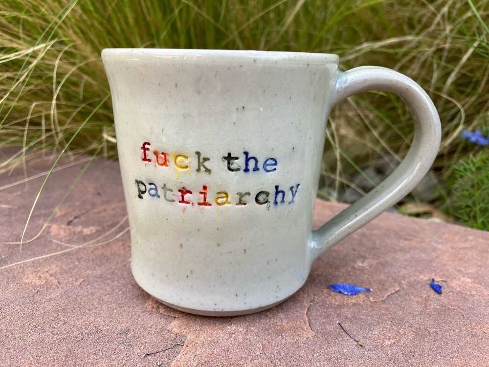 A hand-thrown mug reflects the mood. Fuck the patriarchy in rainbow letters. 