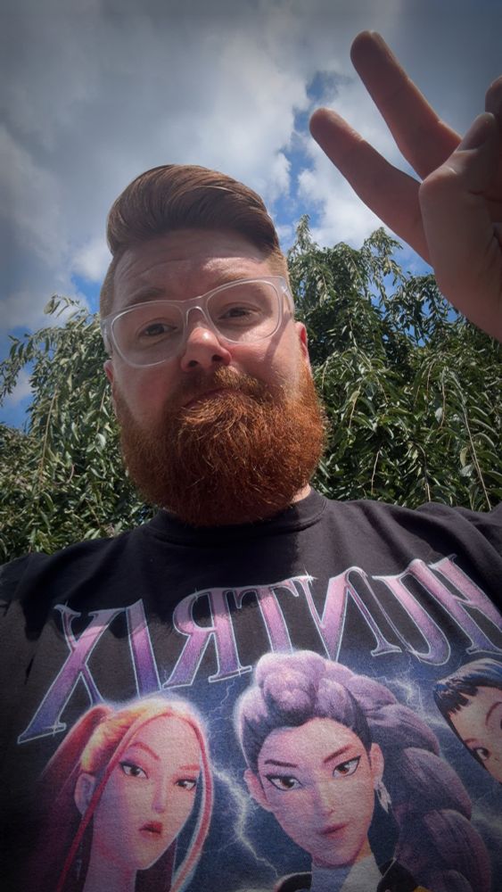 Ginger with a fresh haircut holding a peace sign wearing a black HUNTR/X tshirt