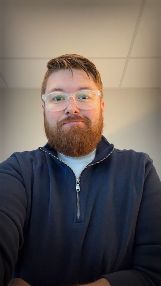 Bearded ginger wearing glasses in a blue quarter zip and white t-shirt