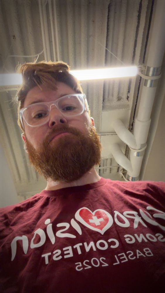 Bearded ginger looking down at your POV in a red shirt