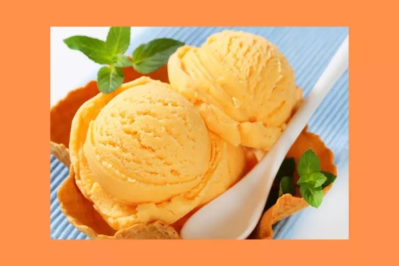 An image of orange sherbet in a sort of waffle cone bowl with little garnishes of some green leafy plant. There is a spoon in the bowl as if it were ready to eat.