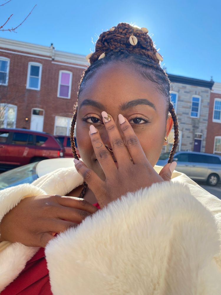 Black woman in fulani braided bun w cowry beads, white coat and red dress