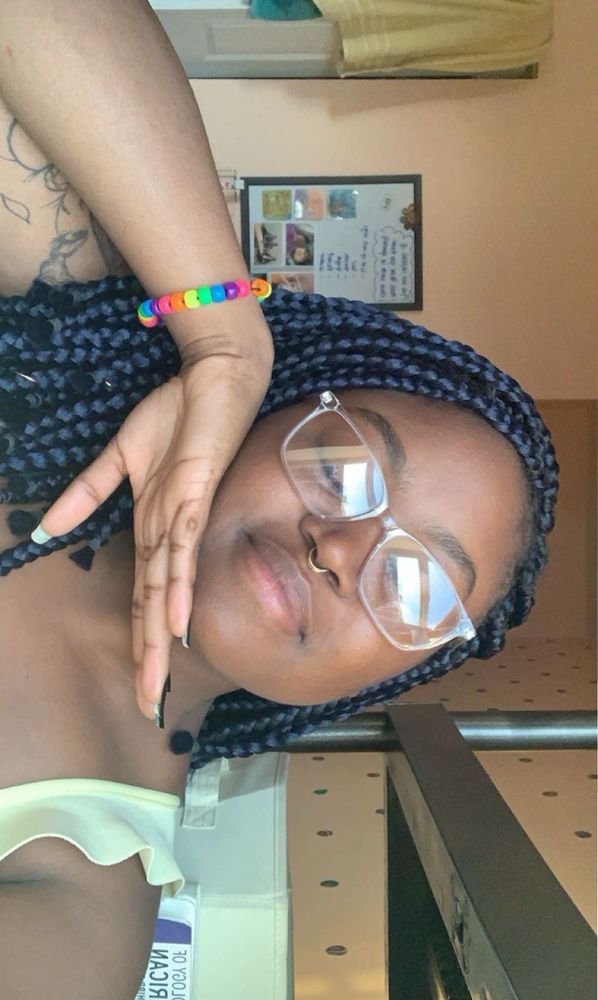 Black woman smiling hand to her face w navy braids wearing a rainbow bracelet