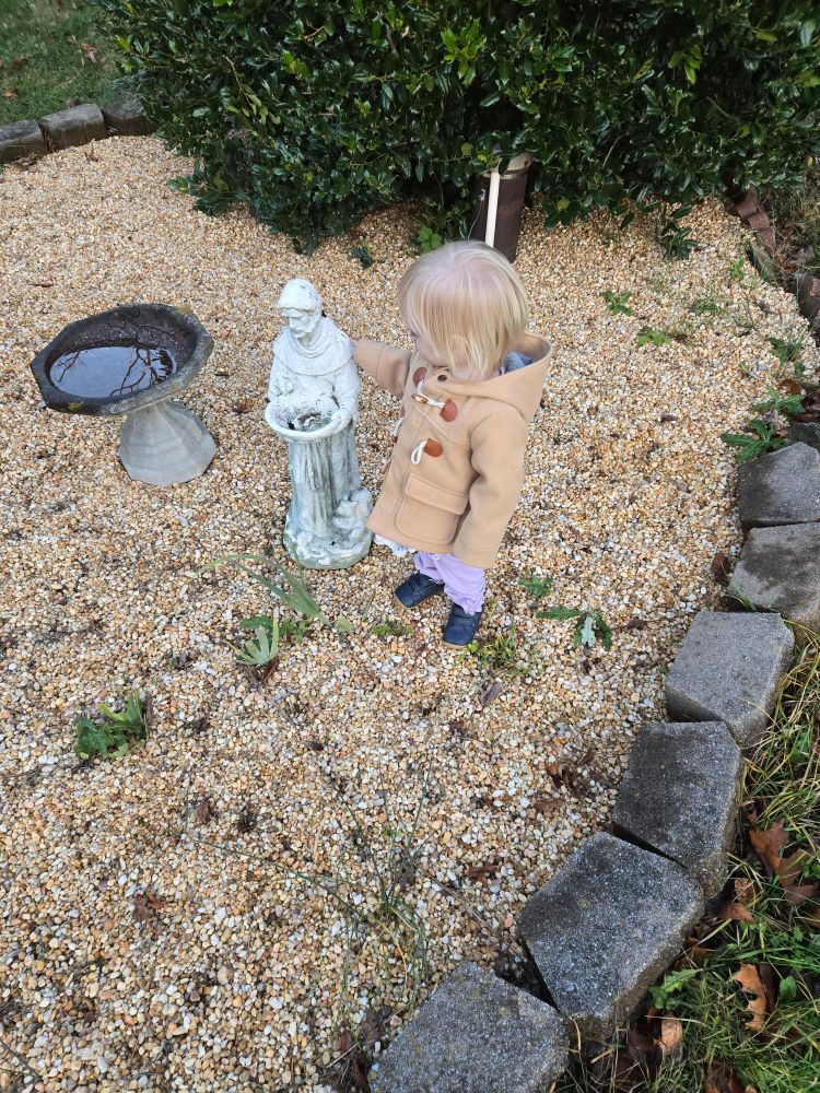 The toddler has her hand on the shoulder of the statue 