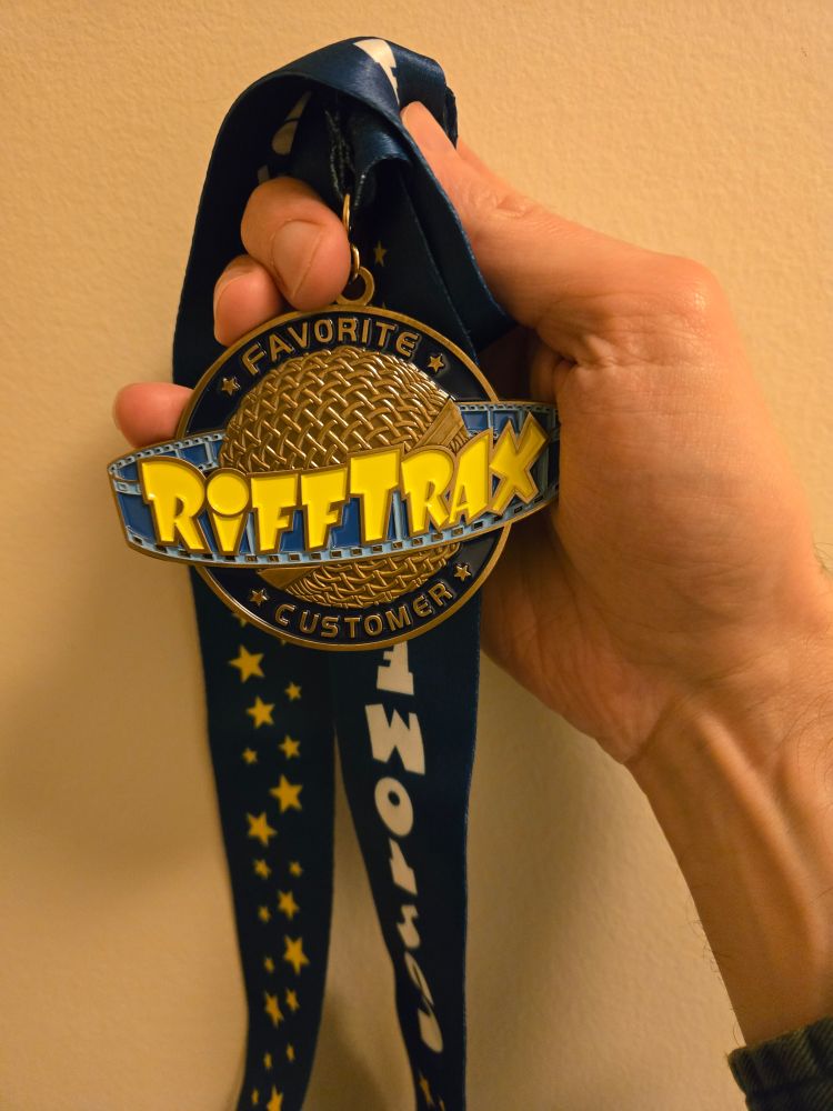 Hand holding a medal that says "Favorite Rifftrax customer" 
