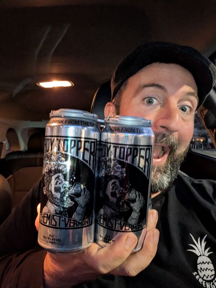 Scruffy young man excitedly brandishes cans of alchemist Brewing heady topper at the camera