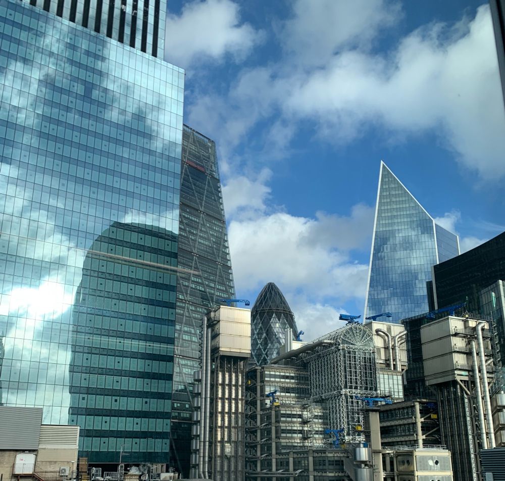 A photograph showing the view from one section of the city of london with blue and cloudy skies, which is heavily occupied by tall buildings including the gherkin and the cheesegrater