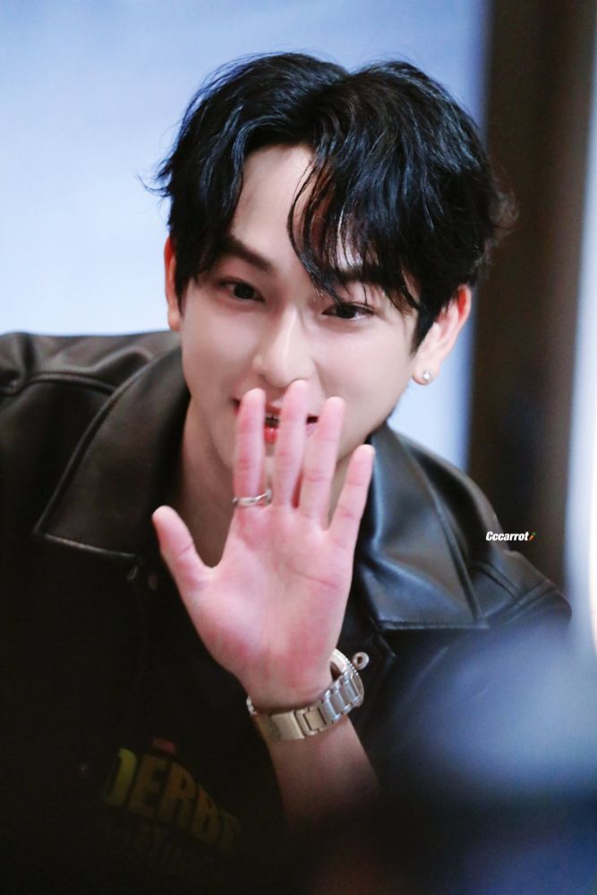Chimon wearing black leather jacket, black t-shirt underneath , black jeans, silver watch, silver ring, and silver small single earring. He’s saying hi to someone 