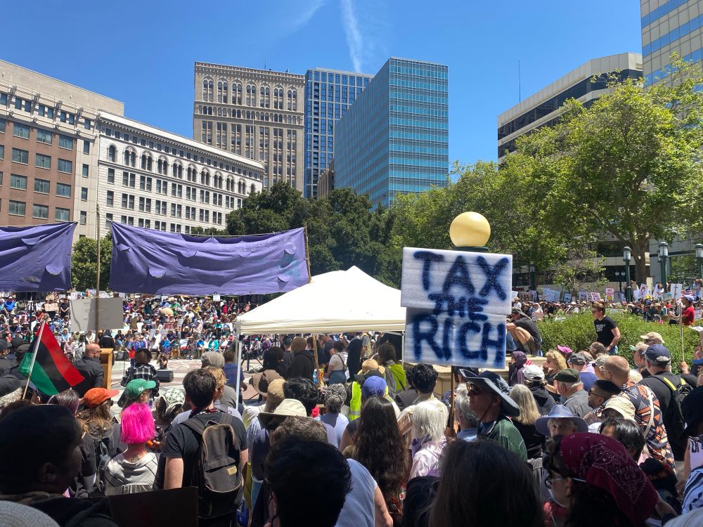 Dense crowds at Frank Ogawa Plaza in downtown Oakland CA June 14, 2025. A sign declares “TAX THE RICH”