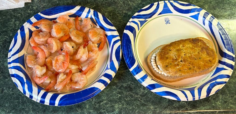 A plate with  pick & peel shrimp on it. 
A plate with oval crab cake on bread with tartar sauce and mayo 