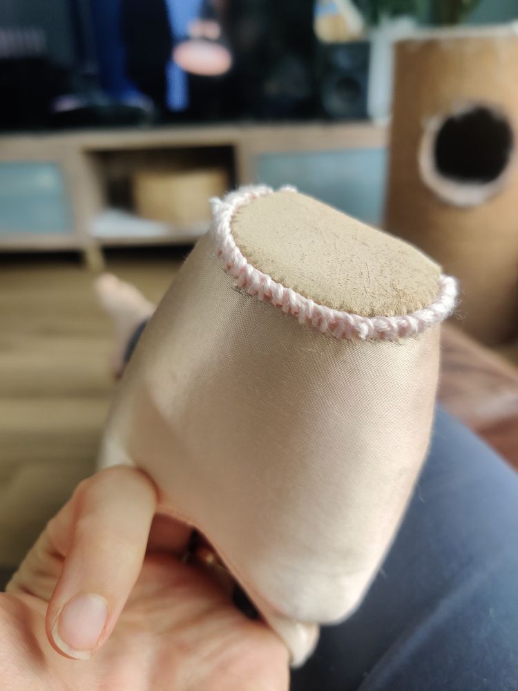 De punt van een Spitz in balletroze satijn. De platte neus waar je op staat heeft een bruin suède stukje en daar omheen een rand van lichtroze katoenen steekjes