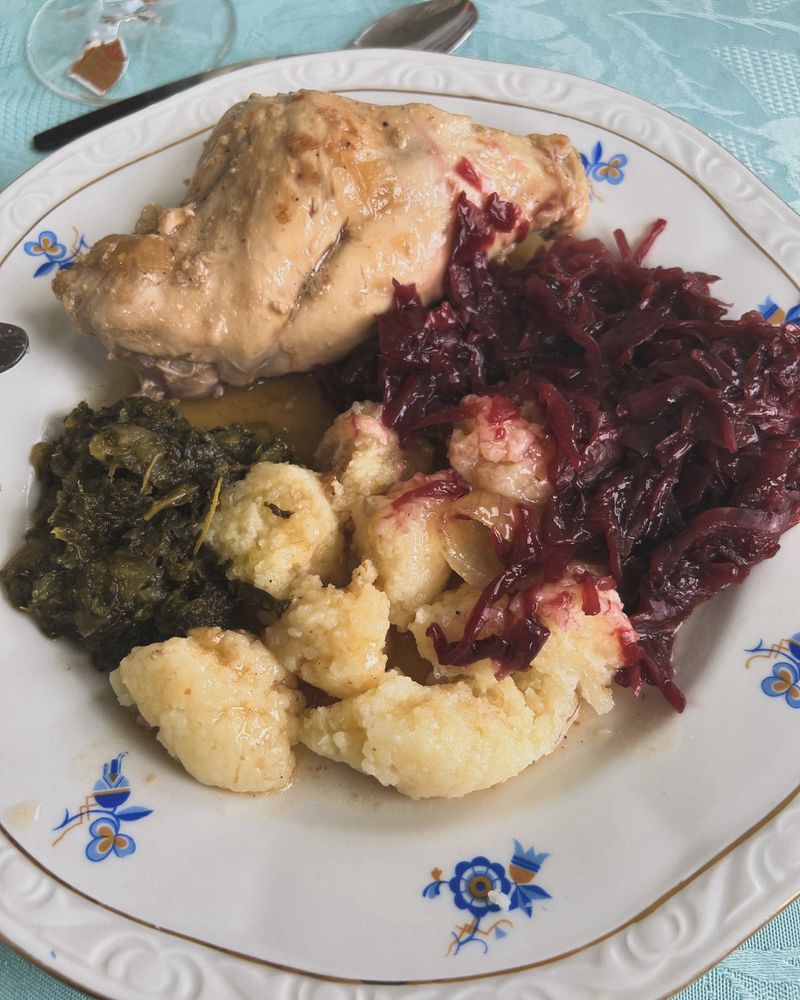 Weißer Teller mit Goldrand und blauen Blumen. Darauf eine Kaninchenkeule, Klöße, Rotkohl, Grünkohl und Soße.
