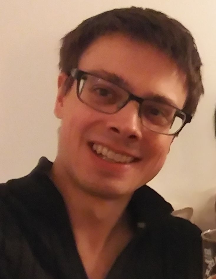 A self-portrait of @skyegek.co in December 2020. She* is wearing a black v-neck sweater, square glasses, and has a simple short haircut.