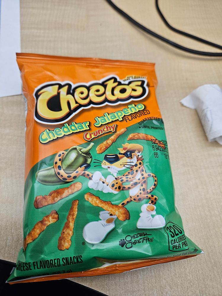 A bag of cheddar jalapeño flavored Cheetos on an office desk top