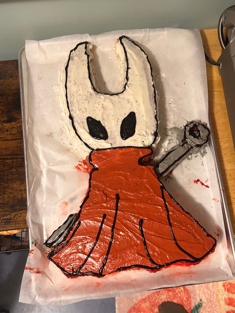 A cake cut and frosted in the shape of hornet from hollow knight. 