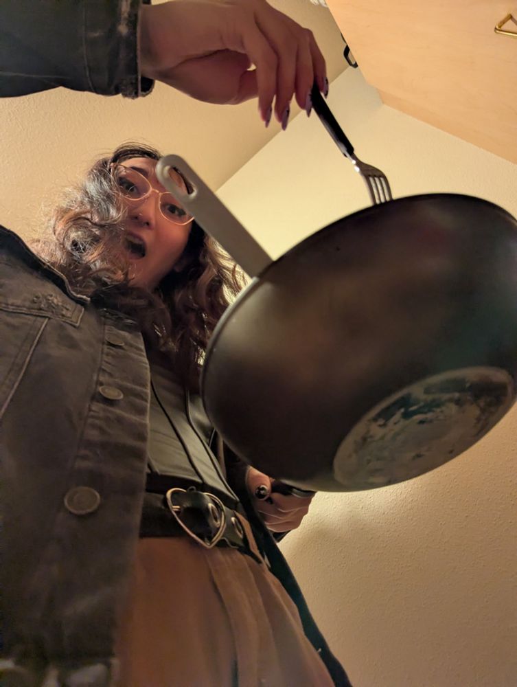 Picture of Maia from below holding a wok in one hand and a fork in the other