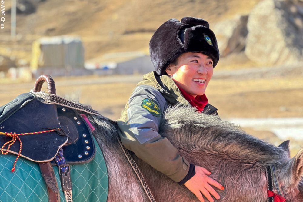 Portrait of Maocuo Yang, the team’s leader petting her horse, while smiling in the bright daylight.