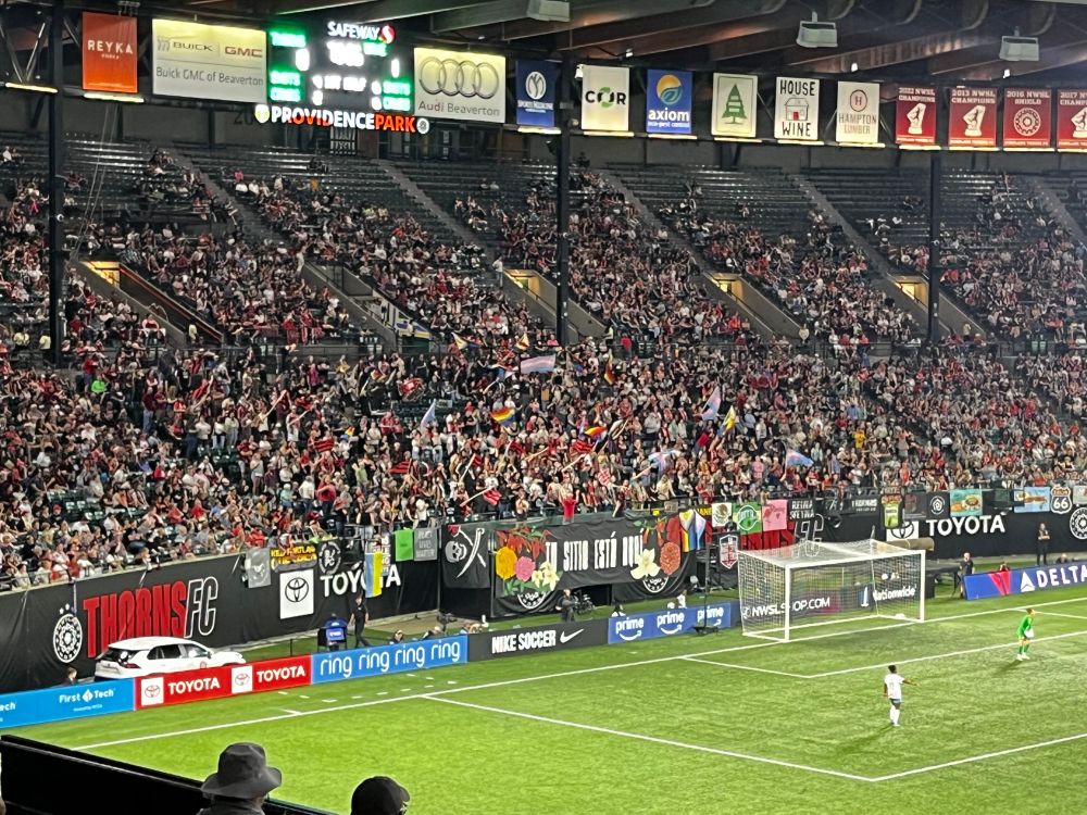 The supporter section at a Portland thorns game, waving flags including a lot of pride flags! 