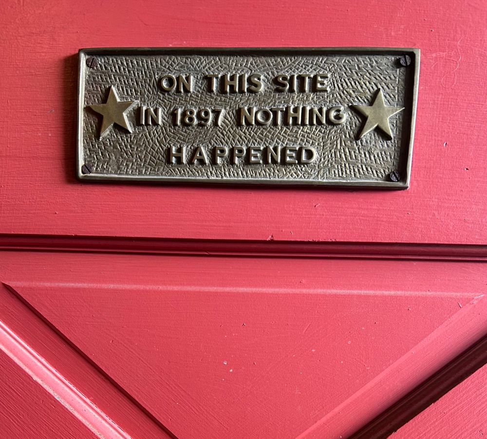 A bronze plaque on a red door says “on this site in 1897 nothing happened.”