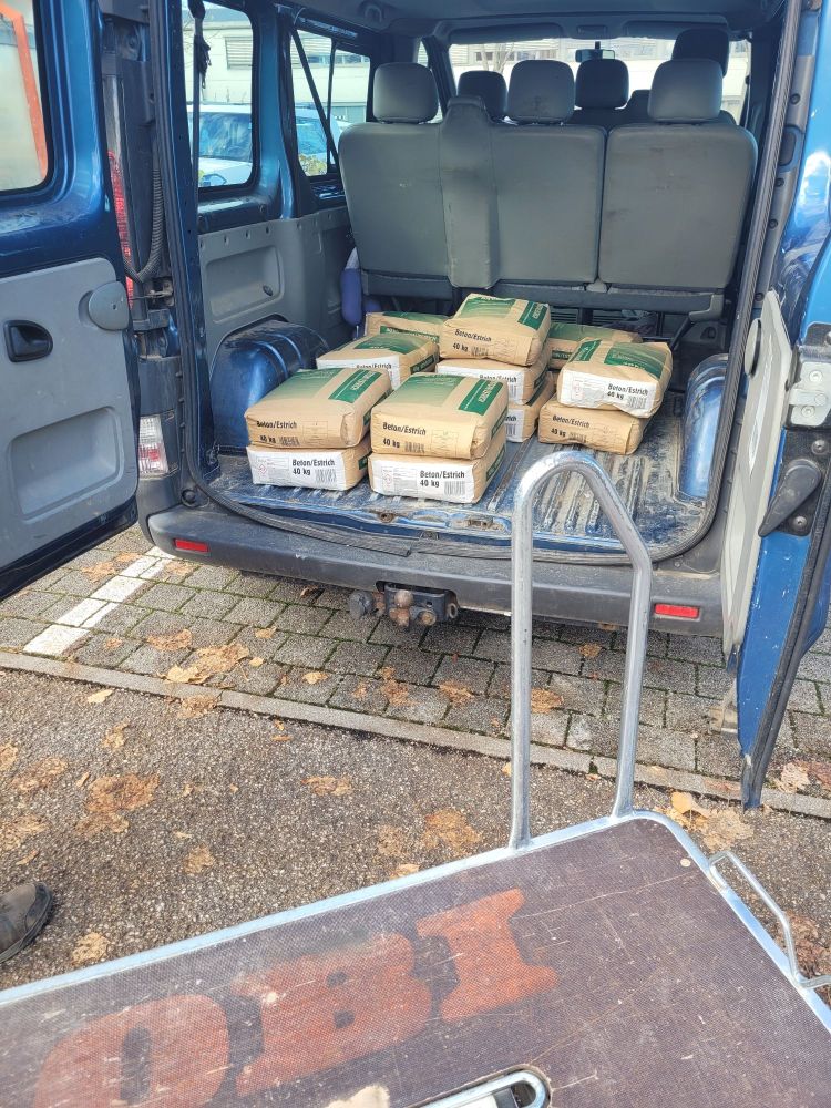 Kofferraum voll mit 15 Betonsäcken, davor Obi-Einkaufswagen