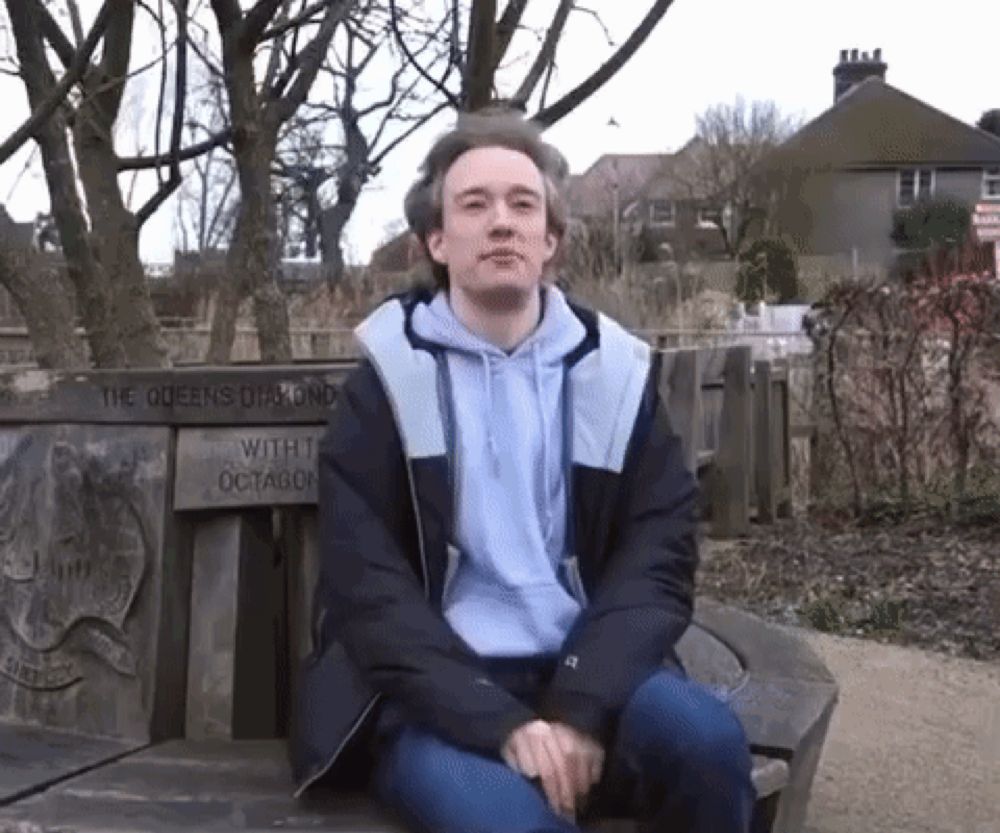 a man sits on a bench with a sign that says the queens round