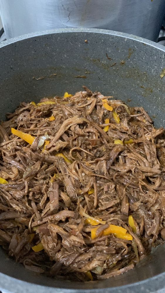 Carne desfiada, carne louca. Em uma panela tem carne desfiada, com cebola e pimentão amarelo. 