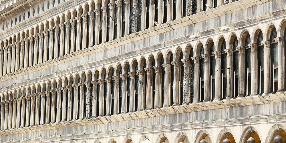 A long facade of narrow, arched windows in the stone wall of an historic building.