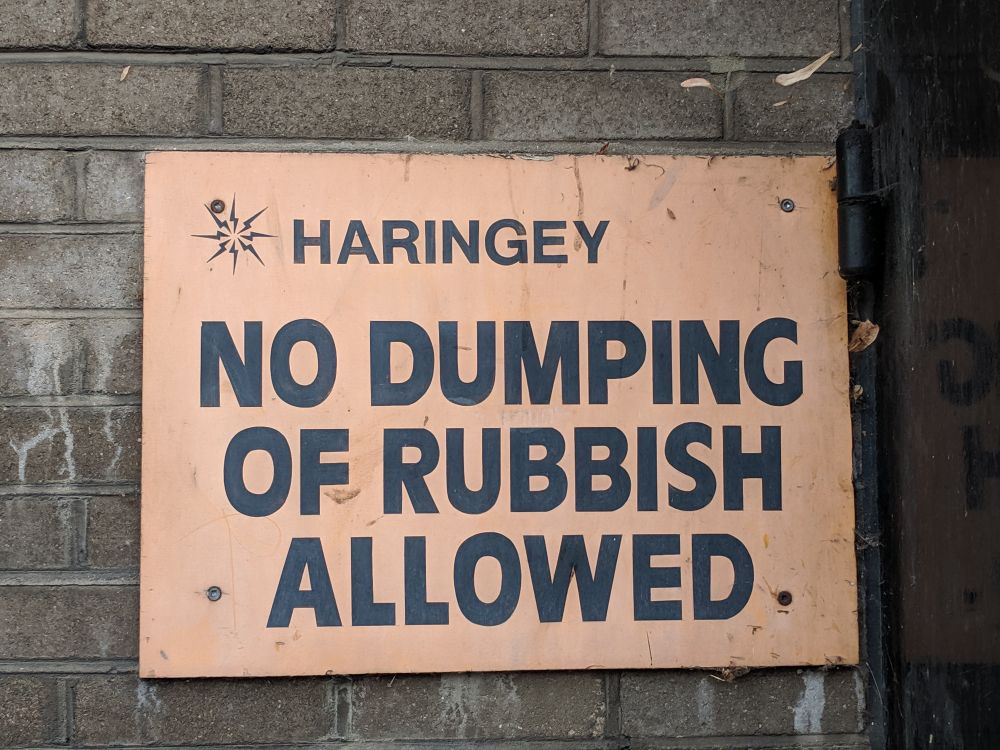 Black on orange, seemingly hand painted with with the original Haringey council logo, and reading NO DUMPING OF RUBBISH ALLOWED 