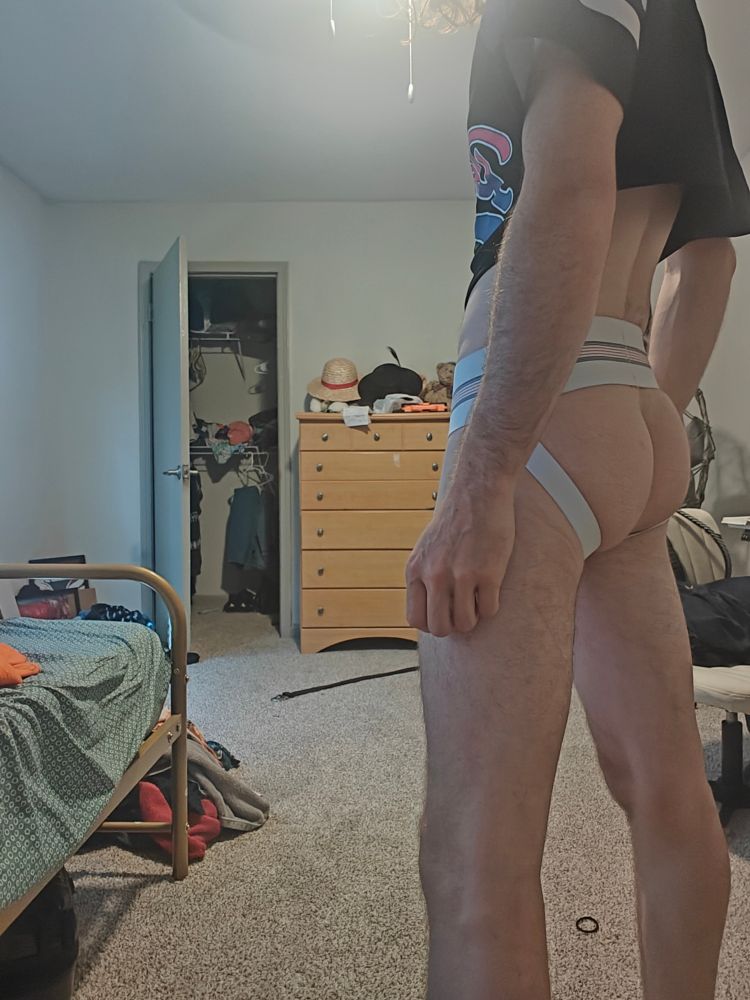 Standing with my arms down in a cropped bisexual pride baseball jersey and a jockstrap showing off more of my ass