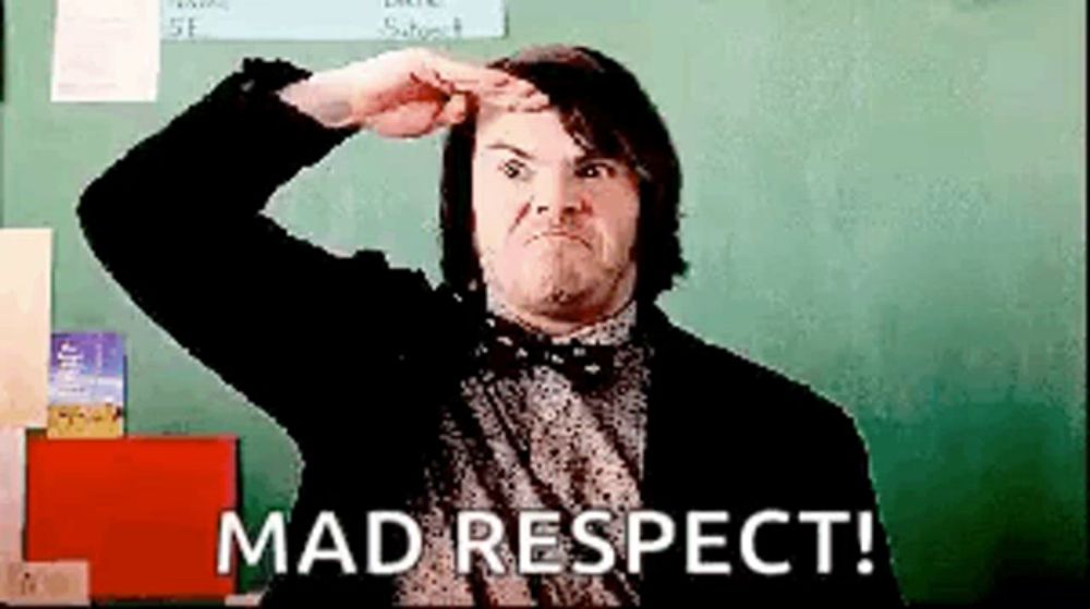 a man in a suit and bow tie is standing in front of a blackboard and making a funny face .