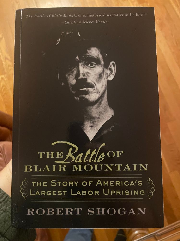 A picture of a softcover book with black cover and gold lettering and a black and white picture of a coal miner with a moustache. The writing on the cover reads “The Battle of Blair Mountain The Story of America’s Largest Labor Uprising”

The author is Robert Shogan