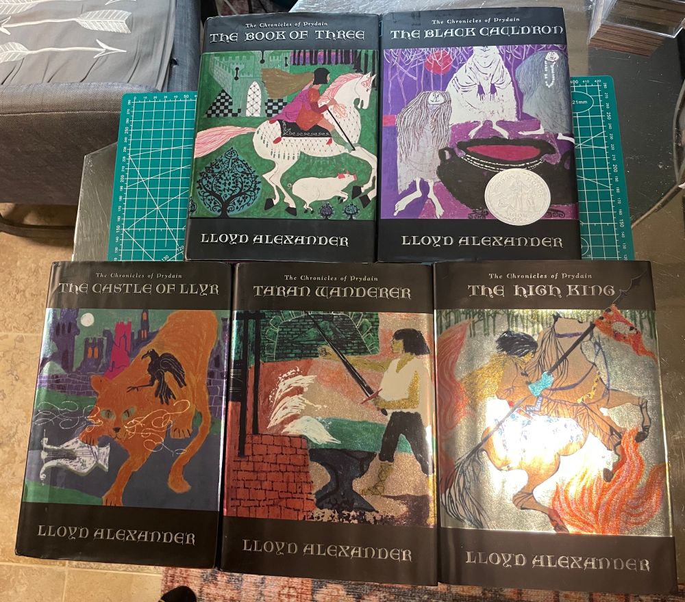 Five hardcover books, the Chronicles of Prydain, with black trim and silver lettering, and center dust jacket art by Evaline Ness, after sticker and Brodart cover removal
