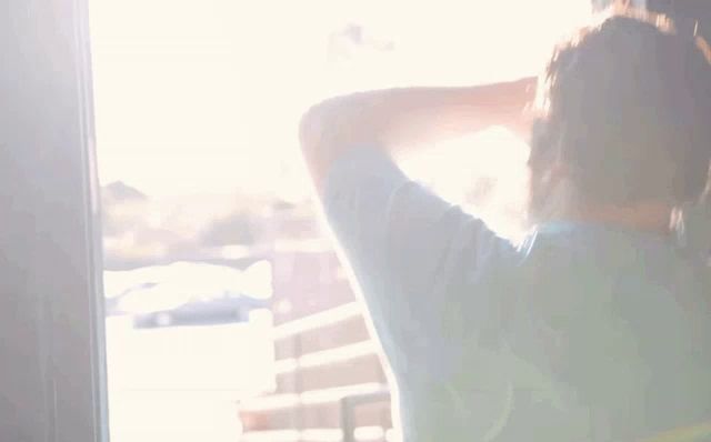 a man with a beard is standing in front of a wall and covering his face with his hand